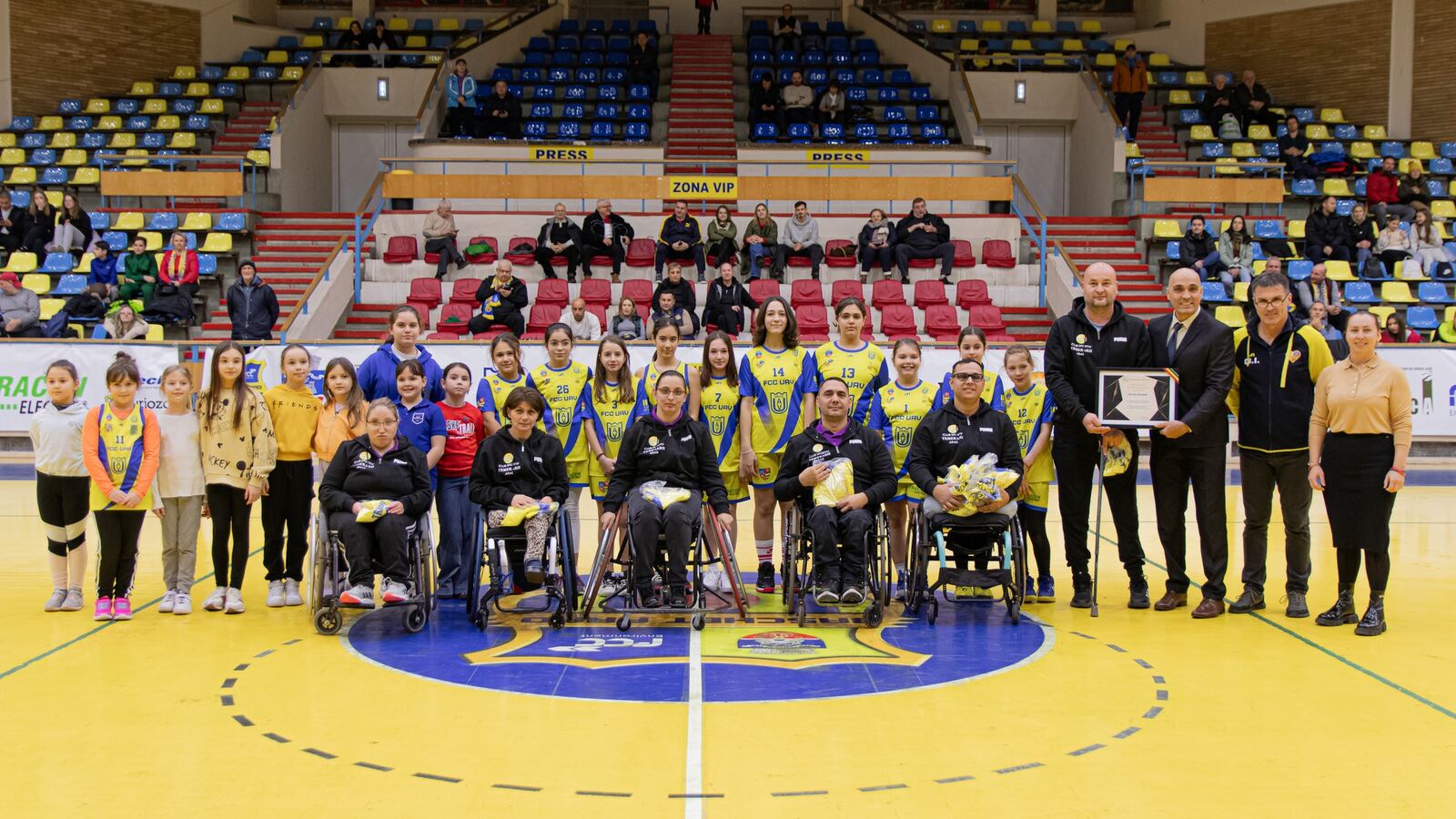 Copiii clubului alături de sportivi de baschet în fotoliu rulant și de oficiali, pe terenul Sălii Polivalente din Arad